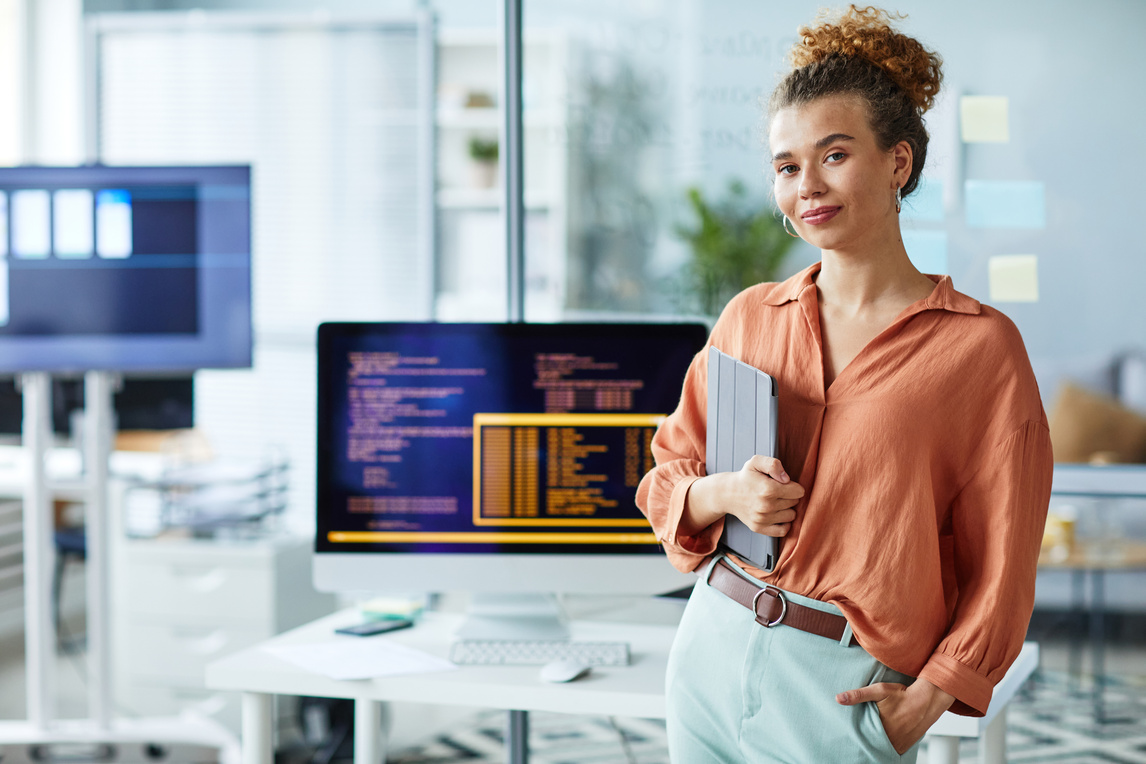 A young woman sitting at a desk with a laptop and looking ahead.